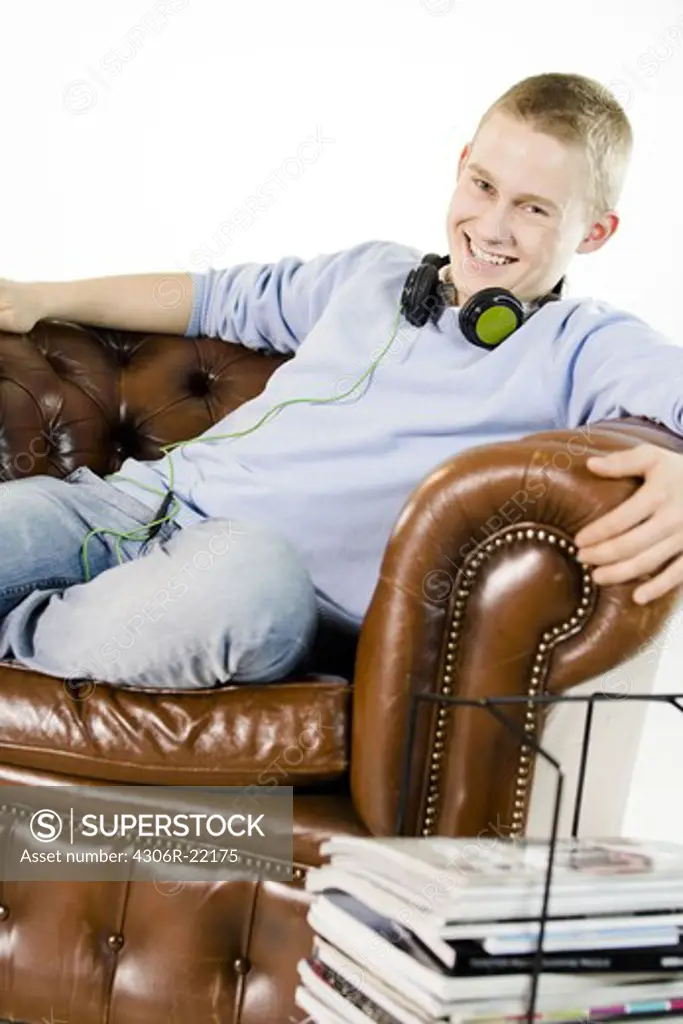 A teenage boy sitting in an armchair using a mobile phone.