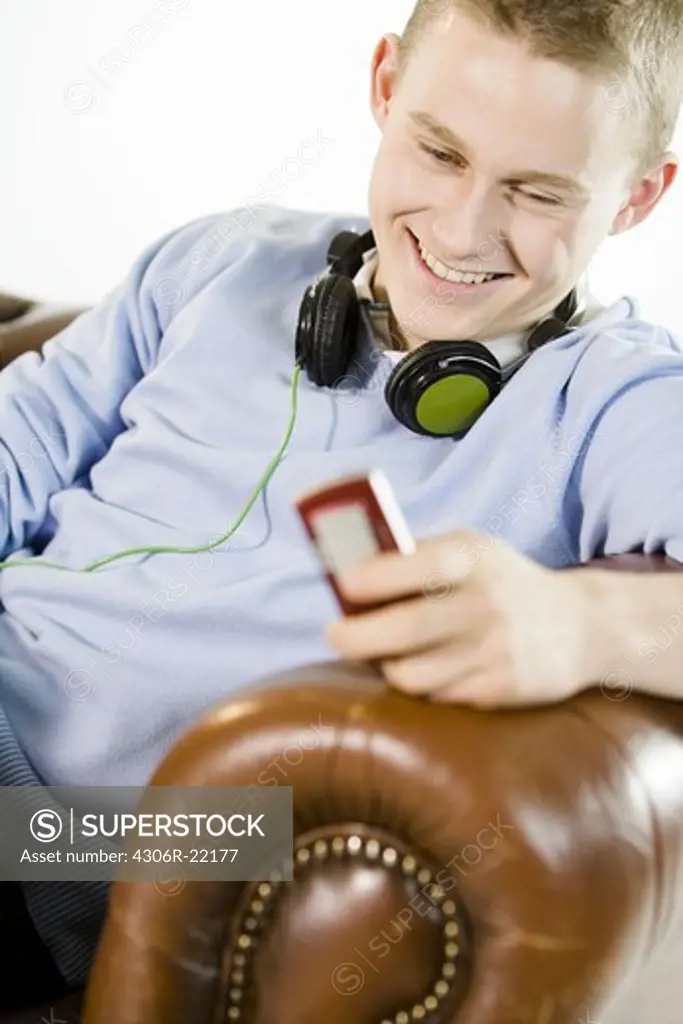 A teenage boy sitting in an armchair using a mobile phone.