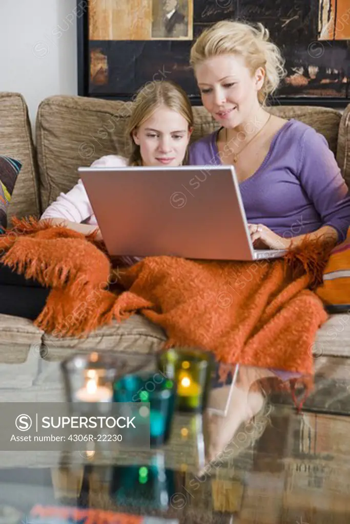 Mother and daughter using a laptop in a couch, Sweden.