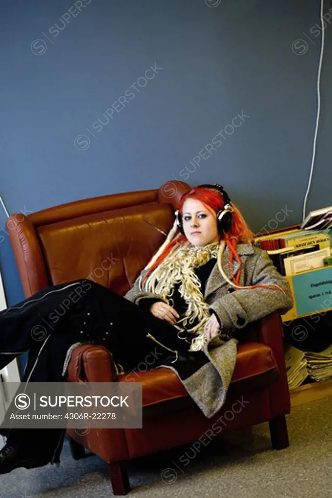Teenage girl with earphones lying in an armchair, Sweden.