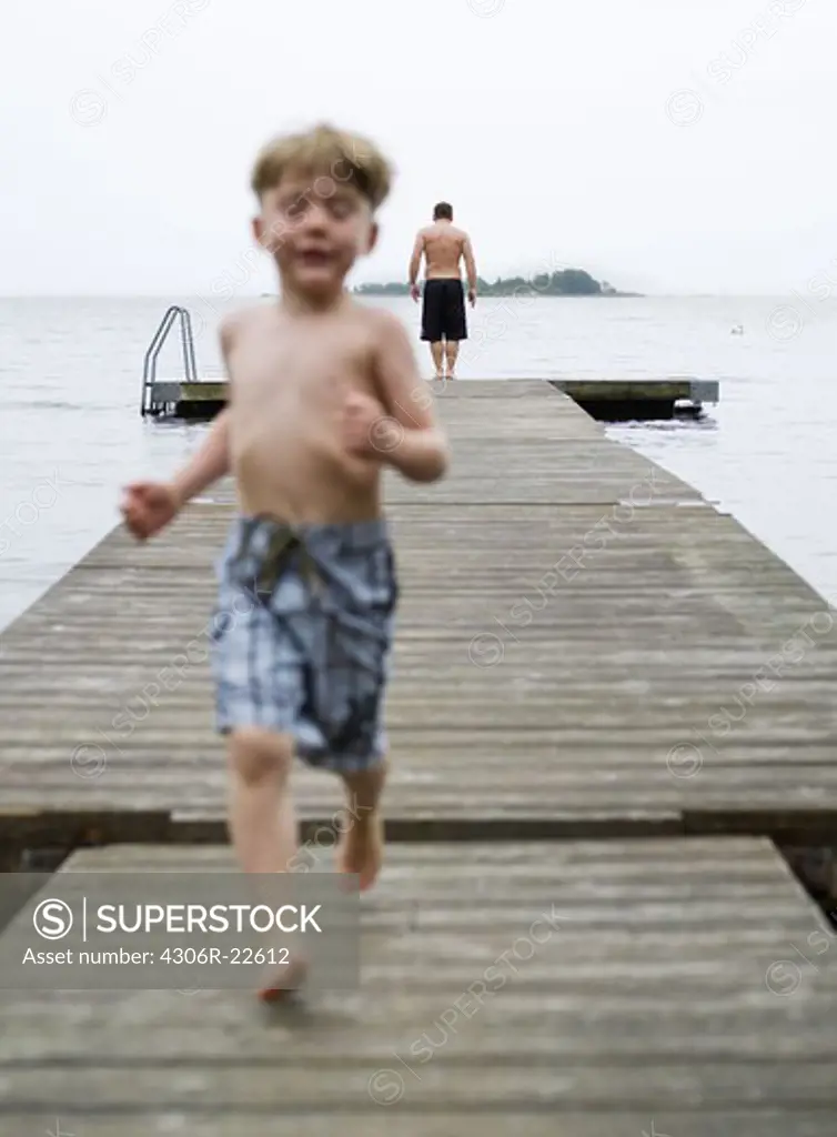 Boy in swimming shorts running on pier