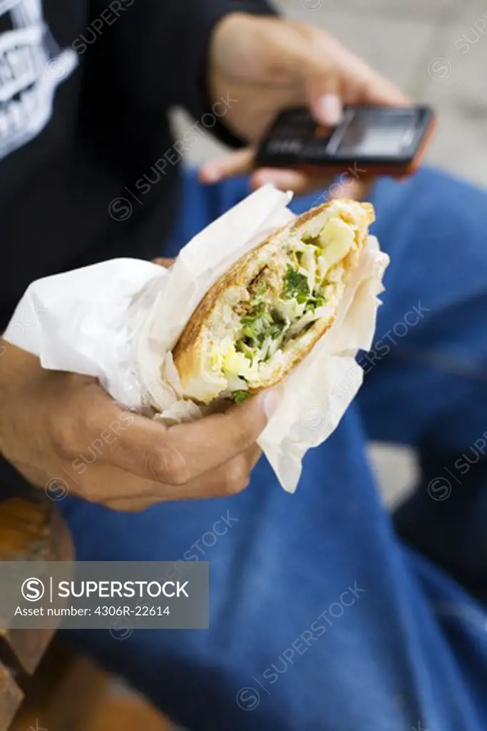 Close up of boys hands holding falafel and mobile phone
