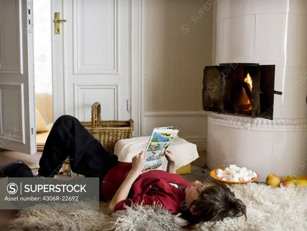 Boy reading by a tiled stove, Sweden.