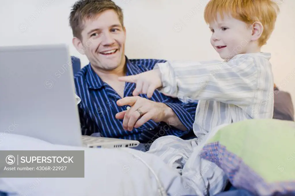 A father and son using a laptop in bed, Sweden.