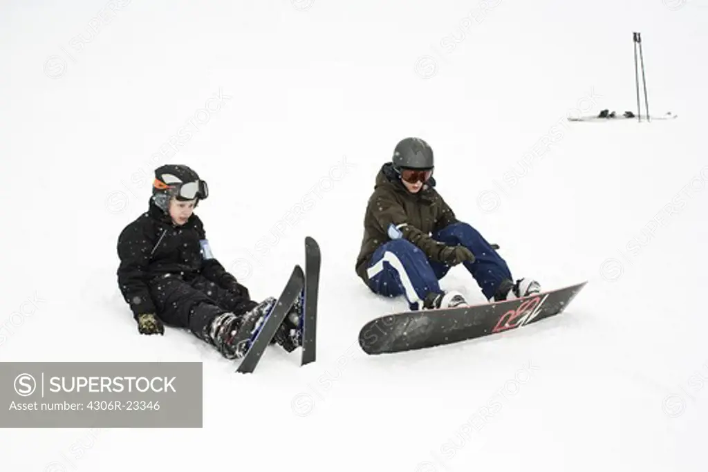 Pair of boys sitting with ski and snowboard