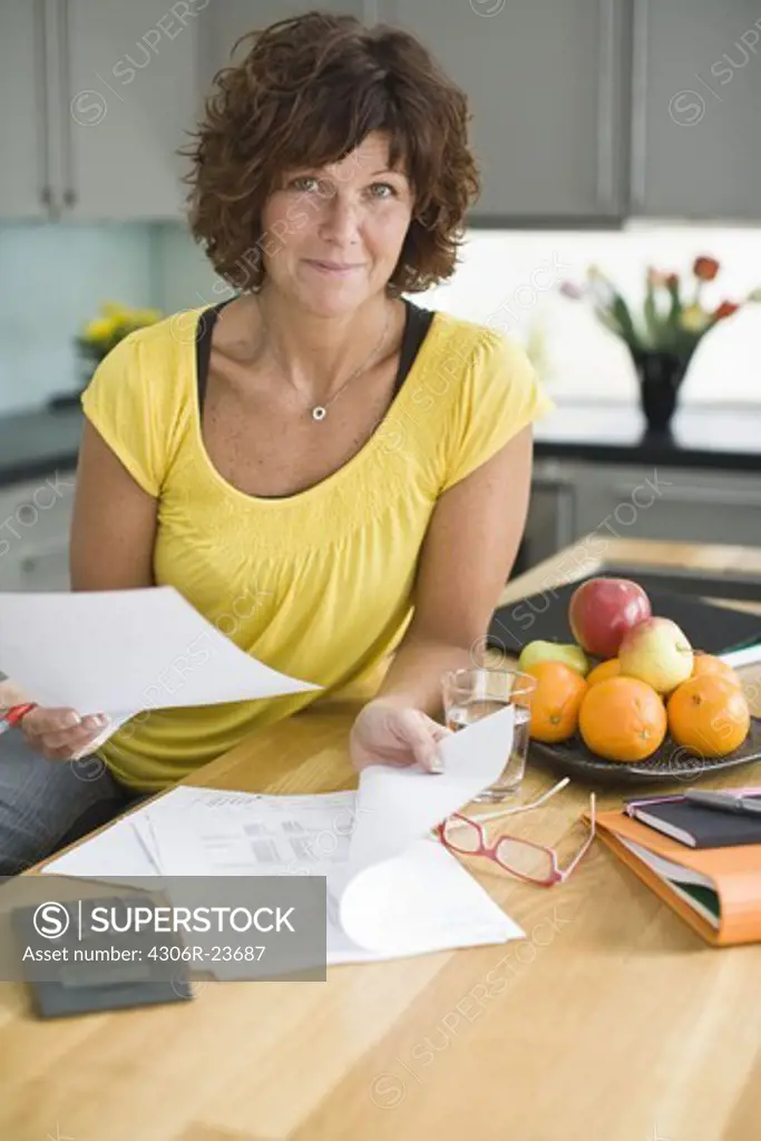 Woman sitting in kitchen with bills, smiling