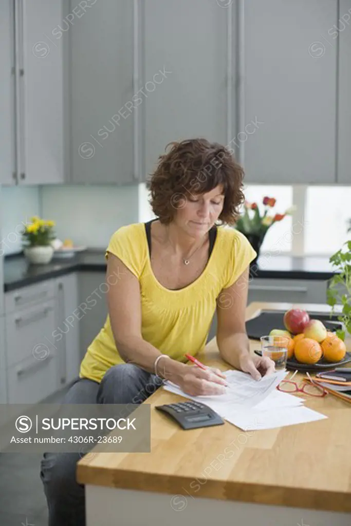 Woman sitting in kitchen with bills