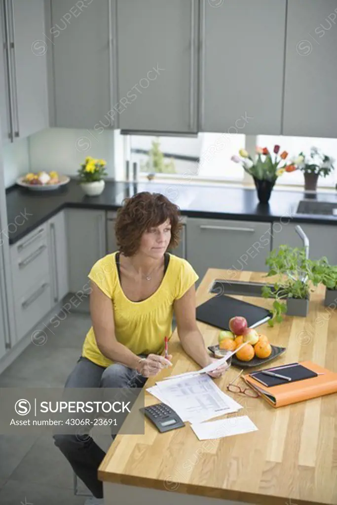 Woman sitting in kitchen with bills