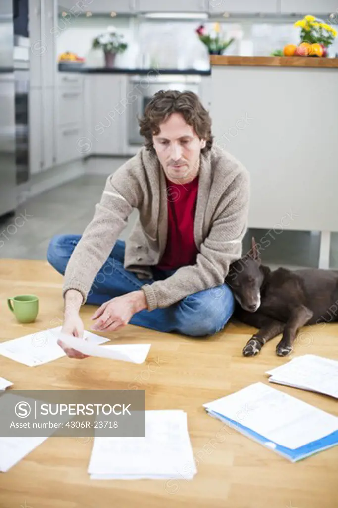 Mid-adult man arranging domestic paperwork on floor, while dog is sleeping next to him