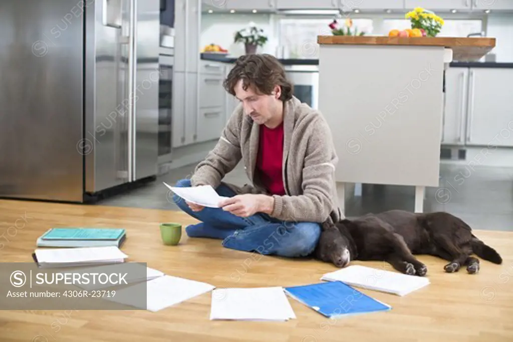 Mid-adult man doing paperwork on floor, while dog is sleeping next to him