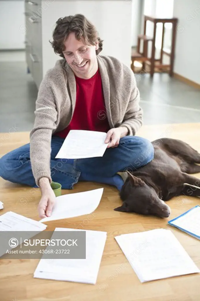 Mid-adult man arranging domestic paperwork on floor, while dog is sleeping next to him