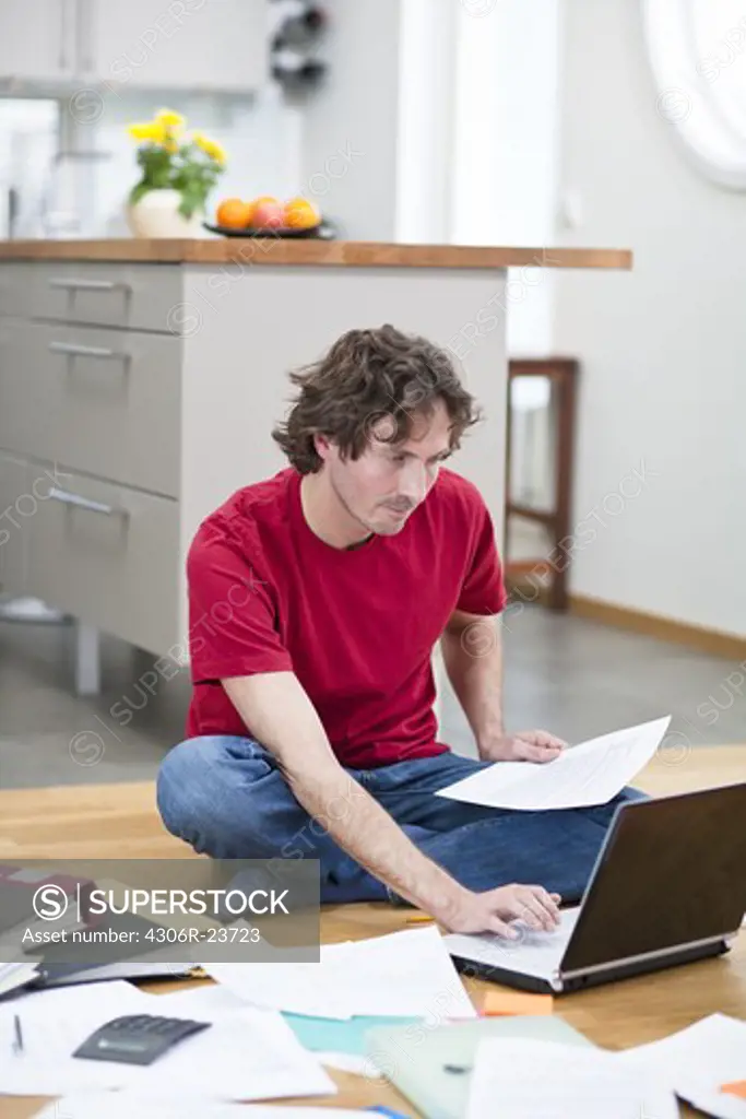 Mid-adult man working from home, using laptop on kitchen floor