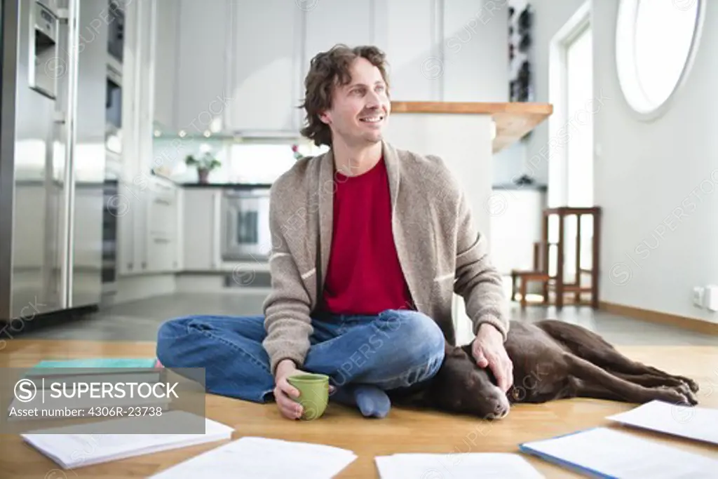 Mid-adult man doing paperwork on floor, while dog is sleeping next to him