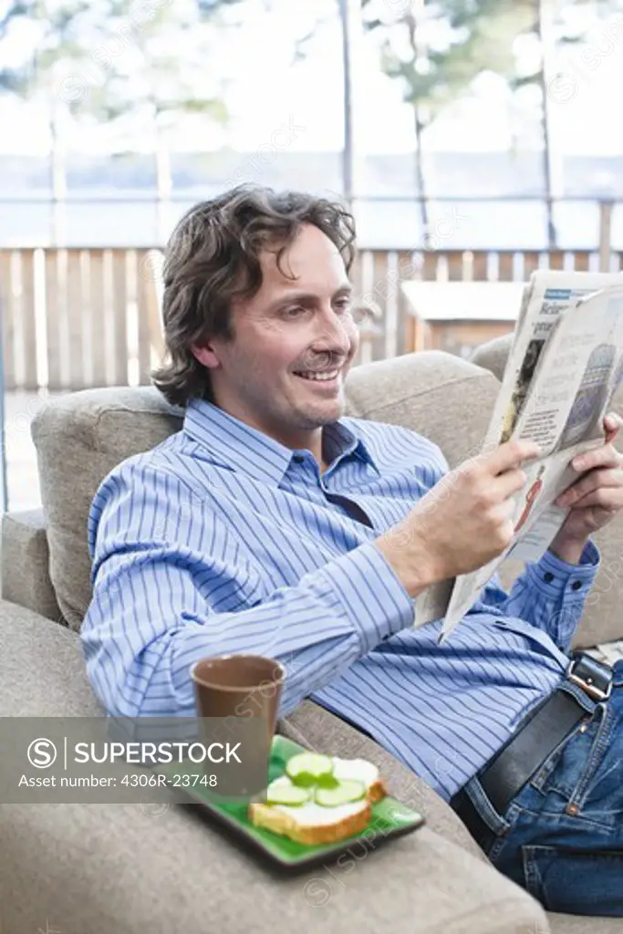 Mid-adult man sitting on sofa, reading newspaper