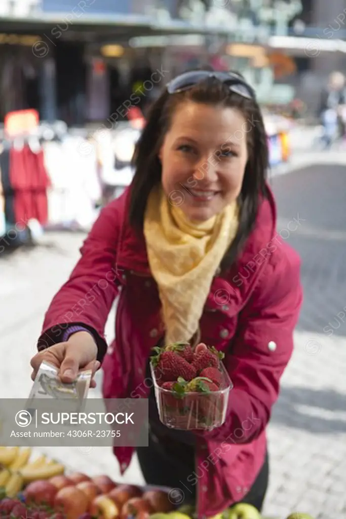 Young woman paying for basket of strawberries