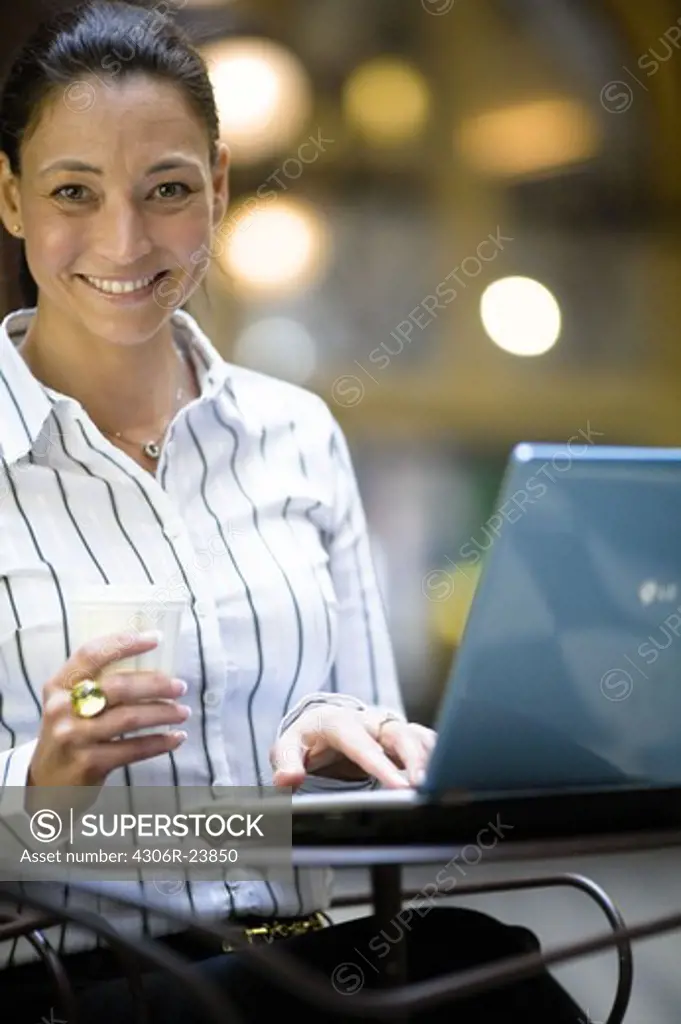 Portrait of mature businesswoman with laptop, holding takeaway coffee