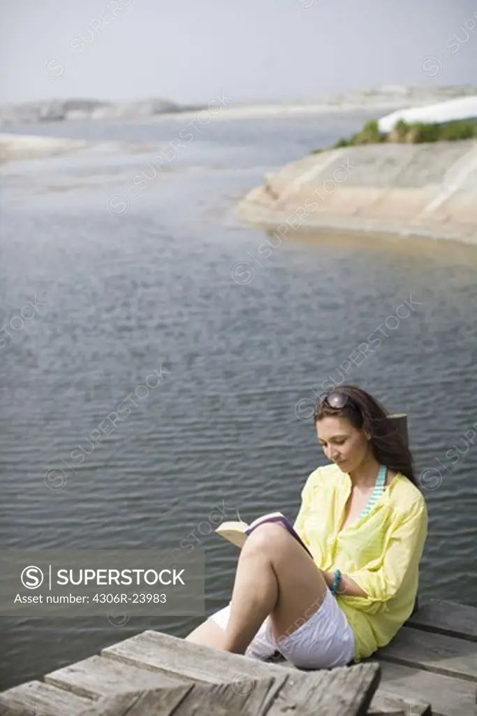 Woman sitting on jetty and reading book