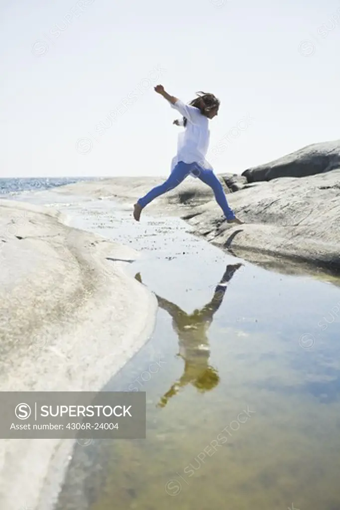 Woman jumping over water to rock