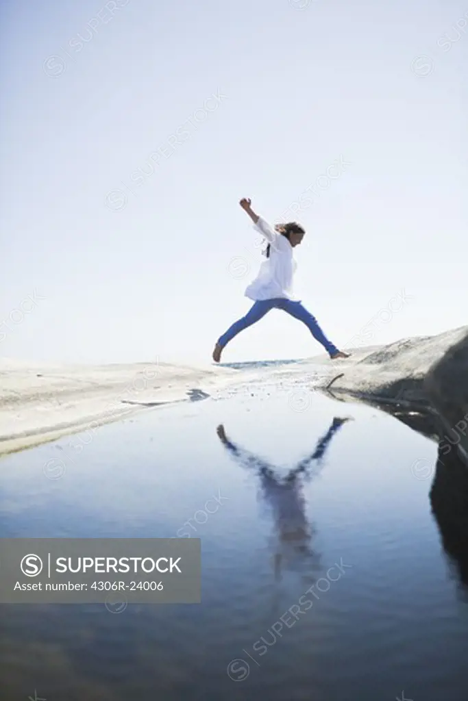 Woman jumping over water to rock