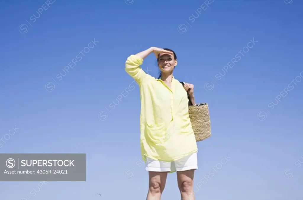 Woman carrying beach bag and shielding eyes