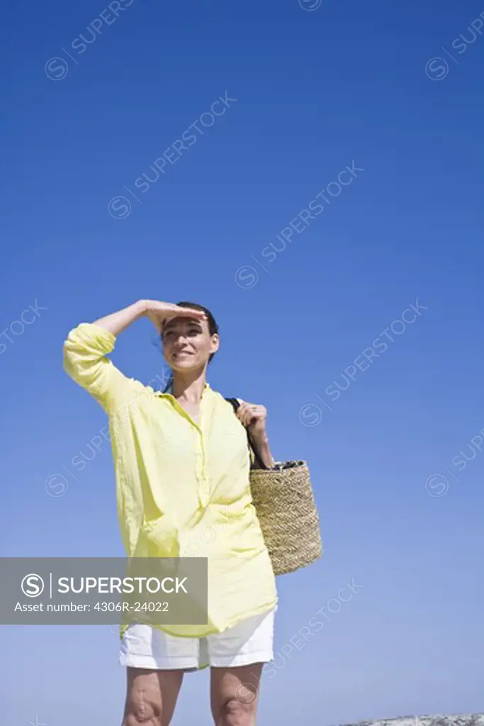 Woman carrying beach bag and shielding eyes