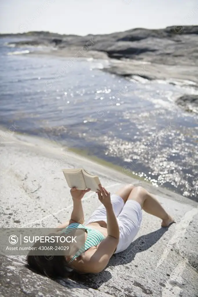 Woman reading book on rock