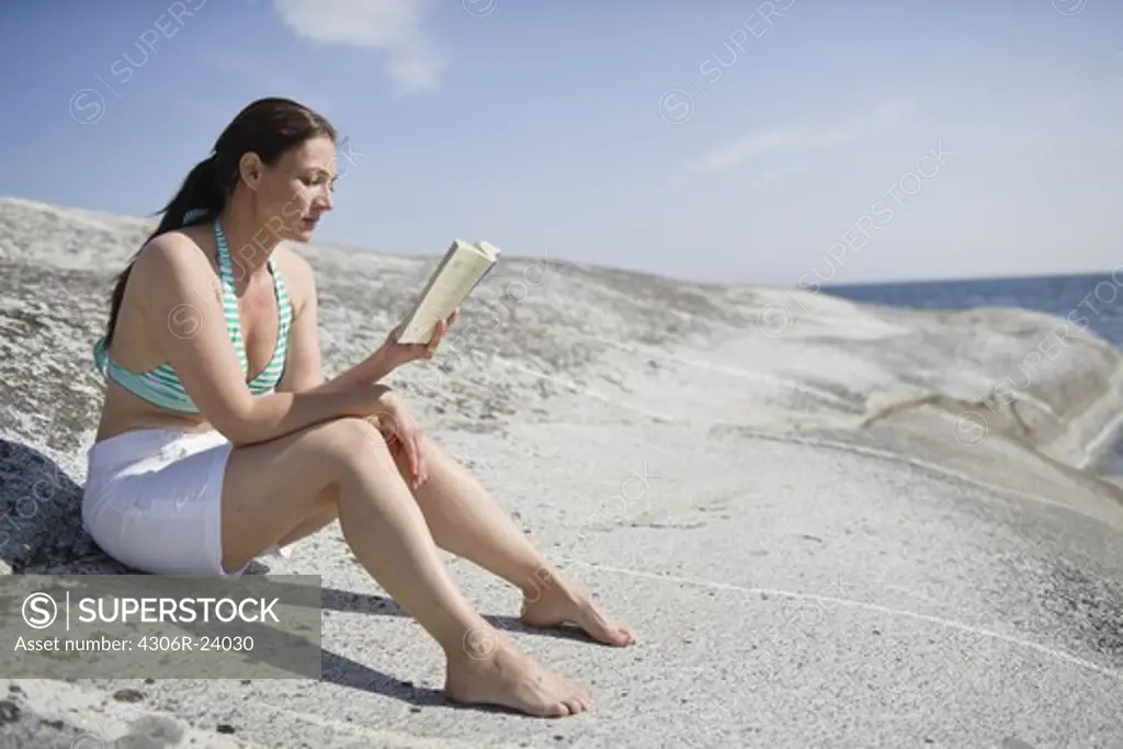 Woman sitting on rock and reading book