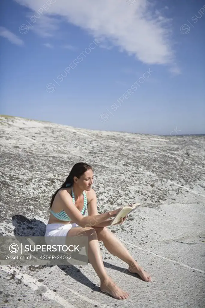 Woman sitting on rock reading book