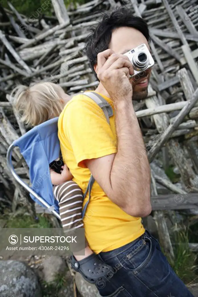 Father carrying daughter in baby carrier, photographing