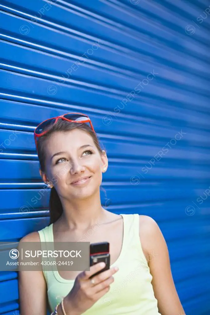 Girl in front of blue wall, holding cell phone