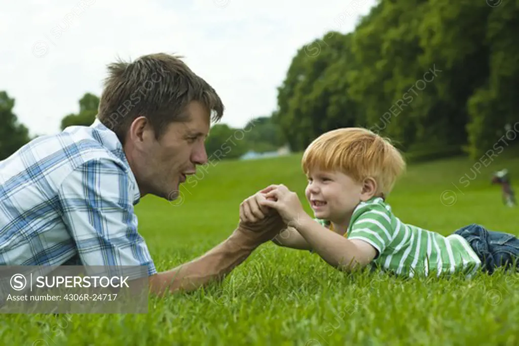 Father and son lying on lawn in park and playing