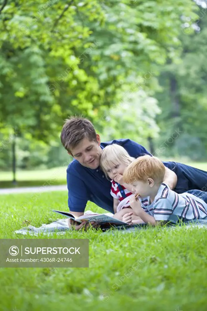 Father reading book to son and daughter in park
