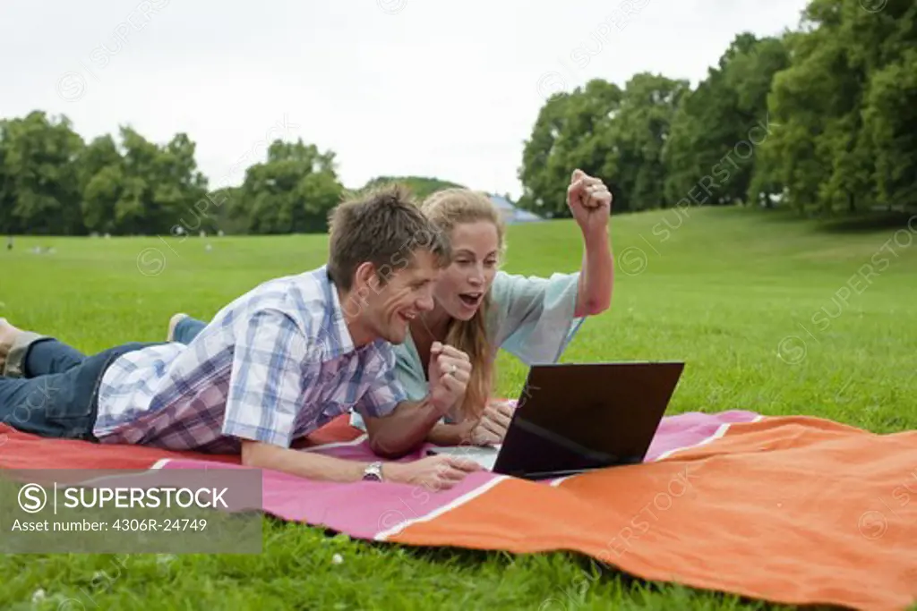 Happy couple lying in park and using laptop