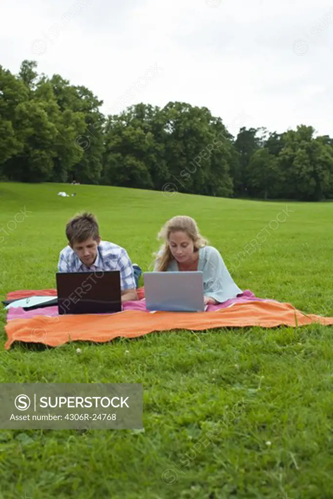 Mid adult couple lying on blanket and using laptops