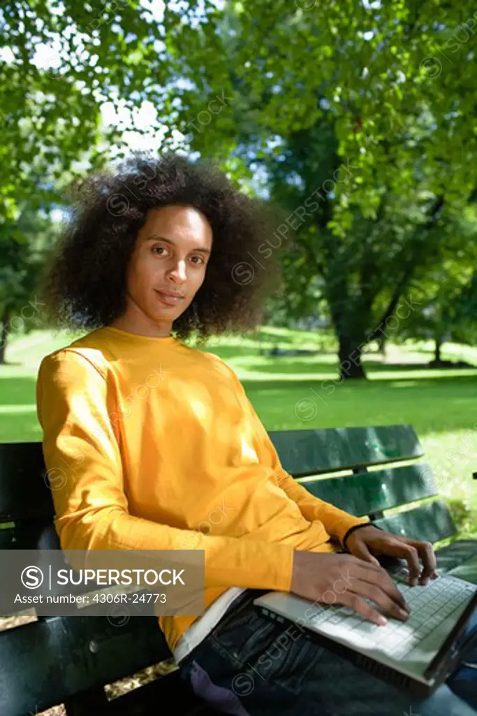 Young man with afro hair sitting on bench with laptop
