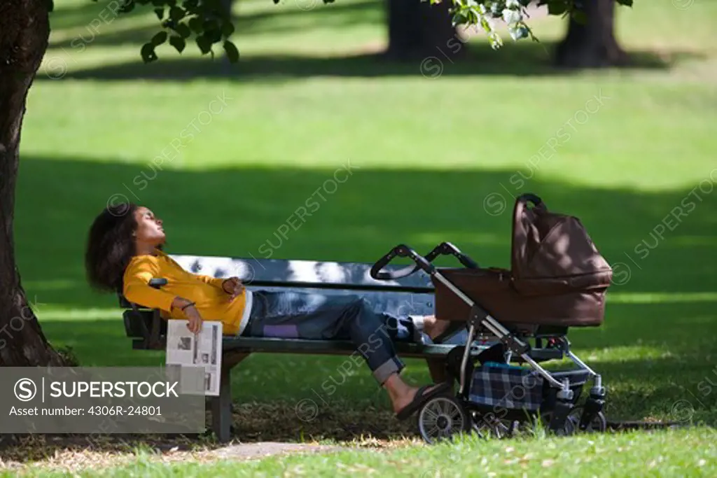 Young man with baby carriage relaxing on bench in park