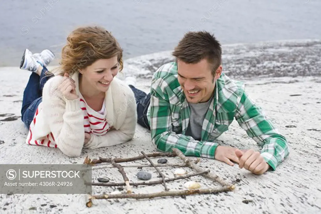 Mid adult couple playing tic-tac-toe on beach