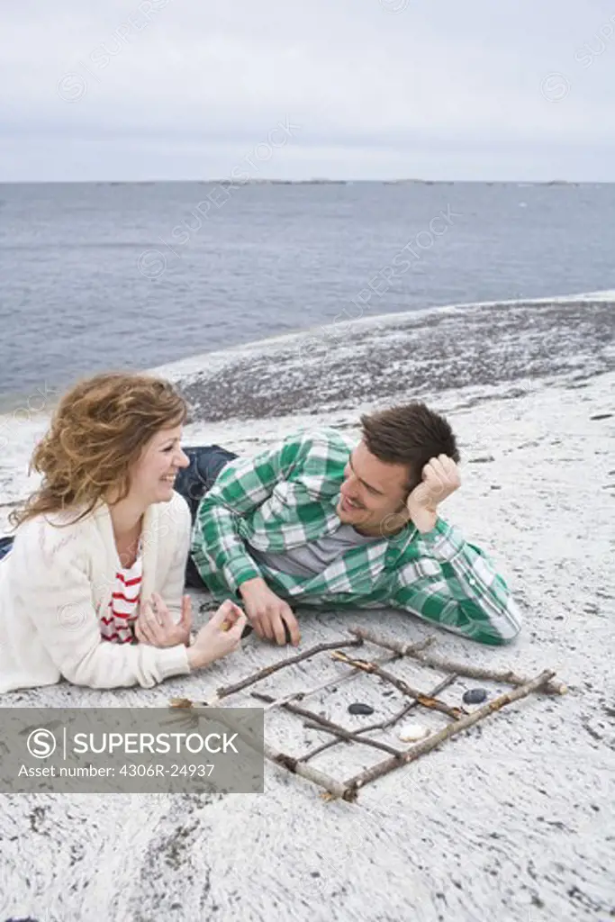 Mid adult couple playing tic-tac-toe on beach