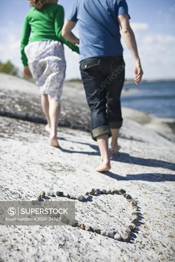 Couple walking away from pebble heart at coast