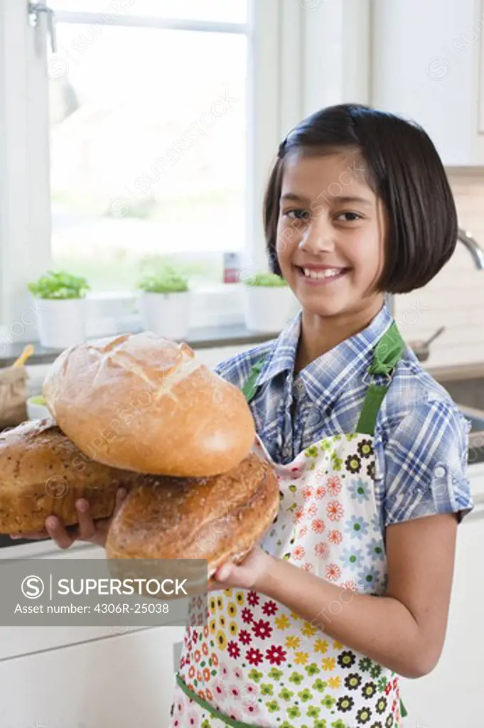 Girl holding loafs of bread, looking at camera and smiling