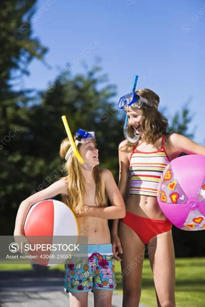 Sisters in scuba mask holding beach balls and looking at each other