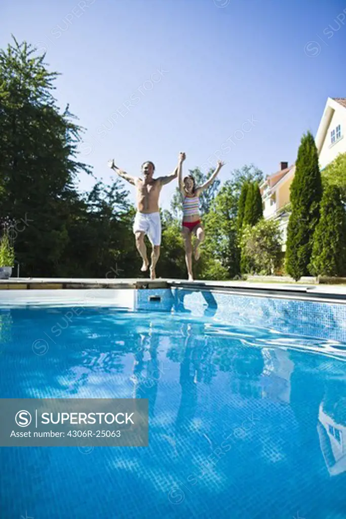 Father and daughter jumping into swimming pool