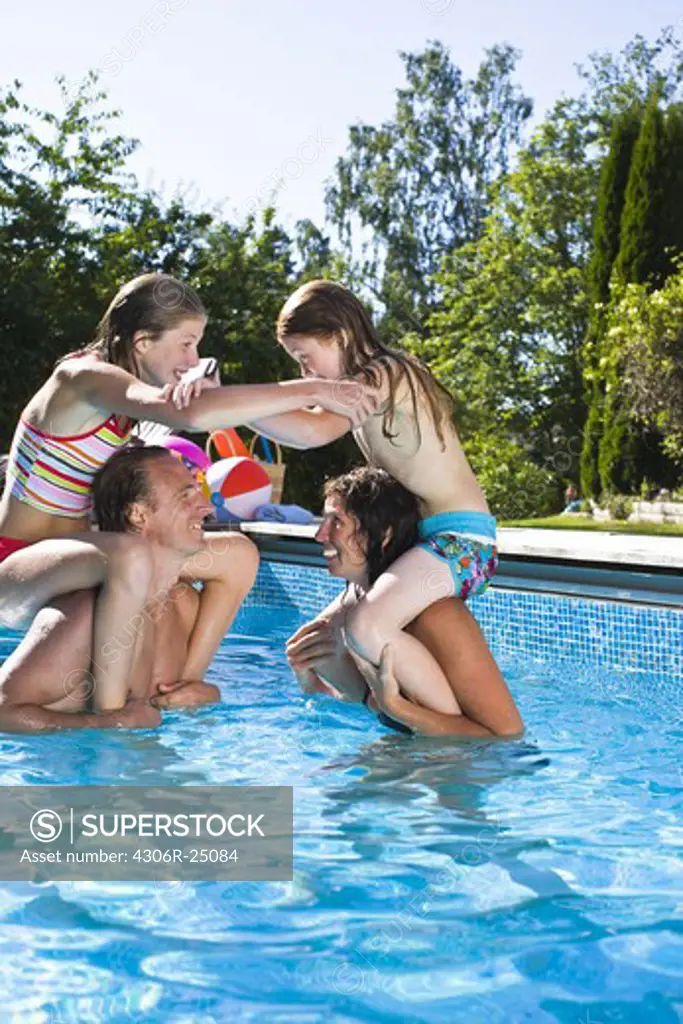 Parent carrying children on shoulders in swimming pool