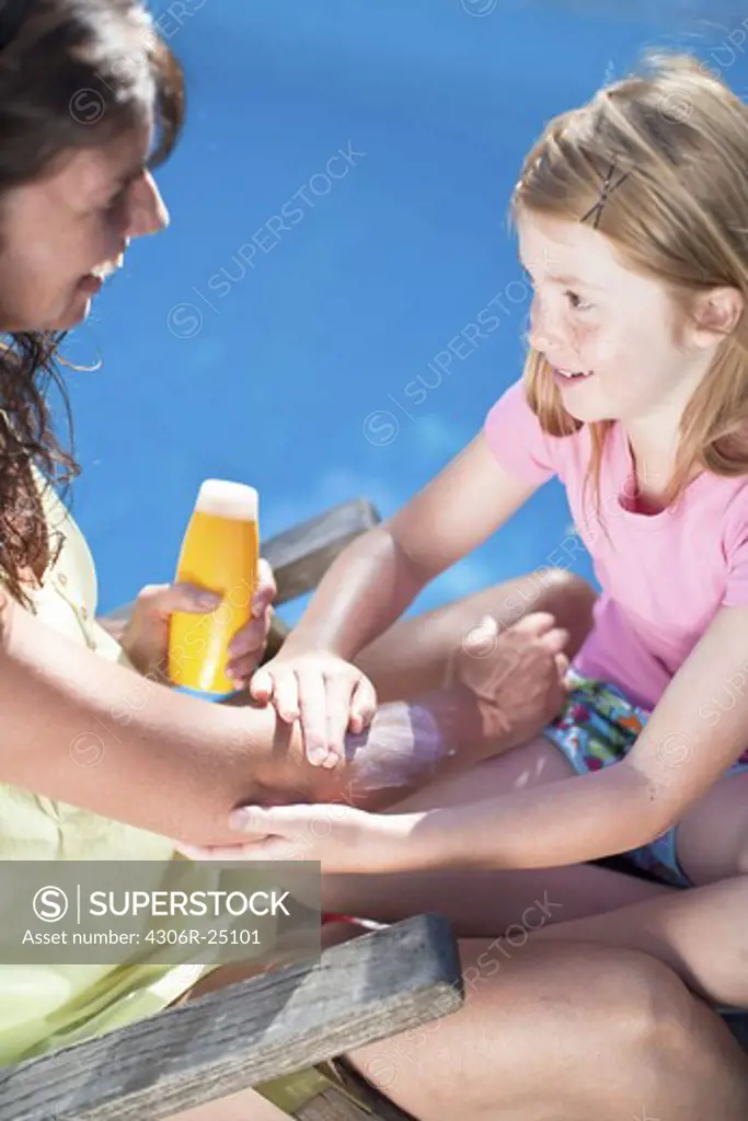 Daughter applying suntan lotion on her mothers arm