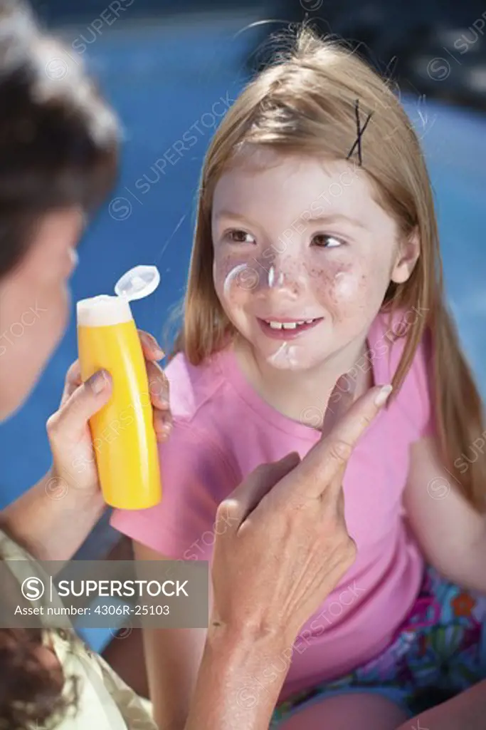 Mother applying suntan lotion on her daughters face