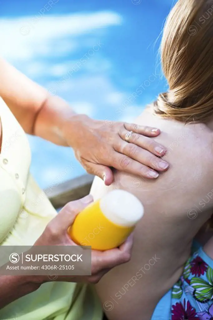 Mother applying suntan lotion on her daughters back