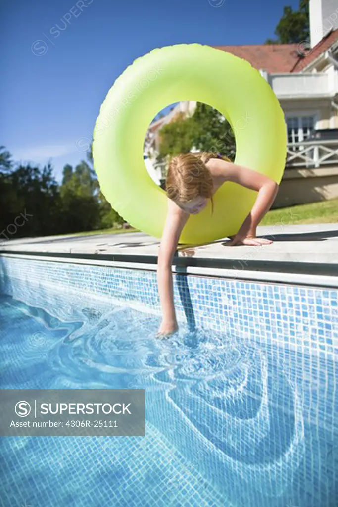 Girl in inflatable ring checking water in swimming pool