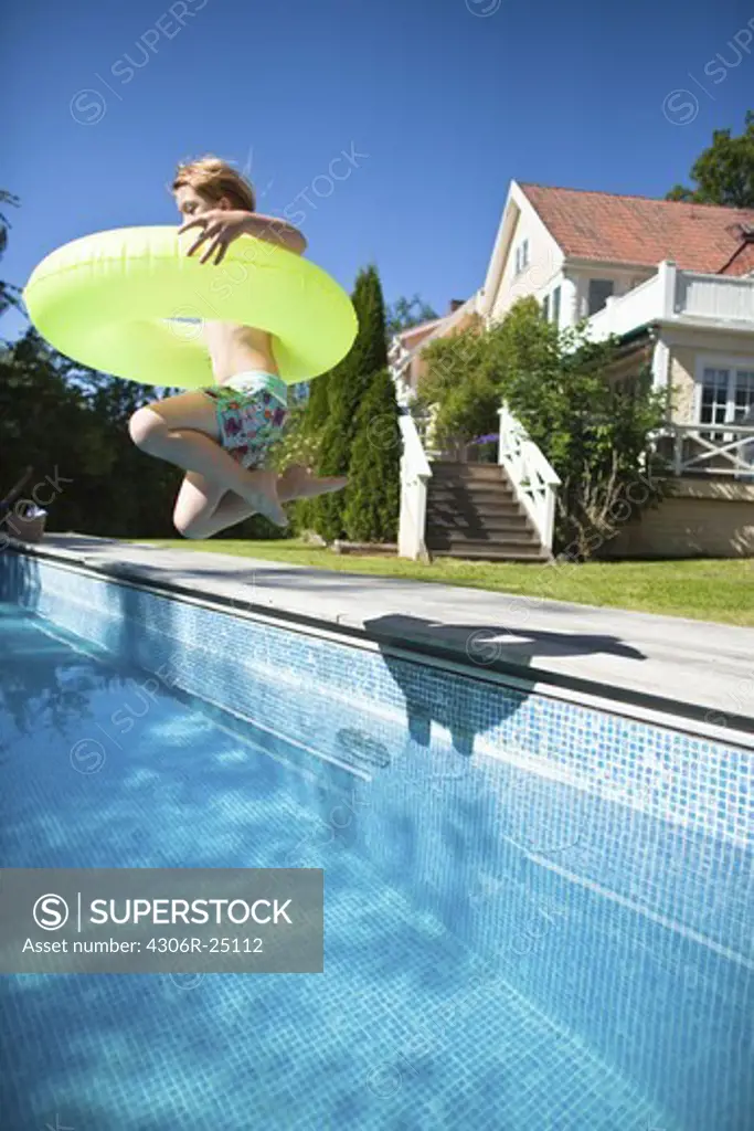 Girl with inflatable ring jumping into swimming pool