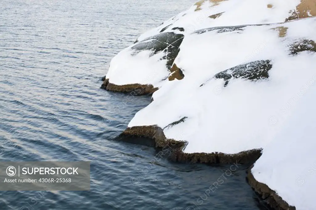 Snow covered rock beside sea
