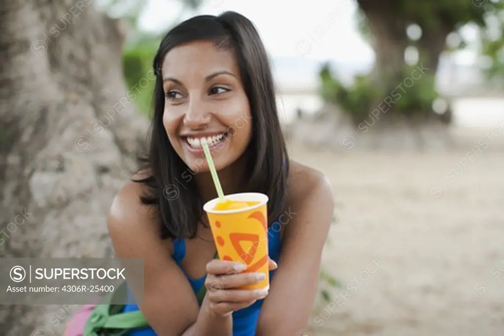 Woman drinking ice cold drink by tree